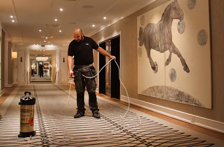 Professional applying Fiber ProTector treatment on luxury hotel carpet for advanced fabric protection and stain resistance.