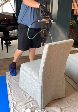 Technician applying Fiber ProTector treatment on upholstered chair for advanced fabric protection and stain resistance in residential interior.