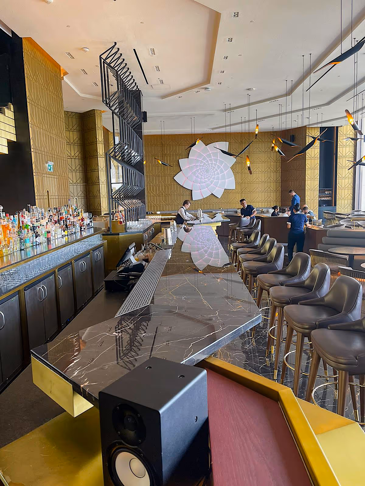 Modern luxury bar interior with marble counter, stylish seating, decorative lighting, and bartender serving guests in an upscale restaurant setting.