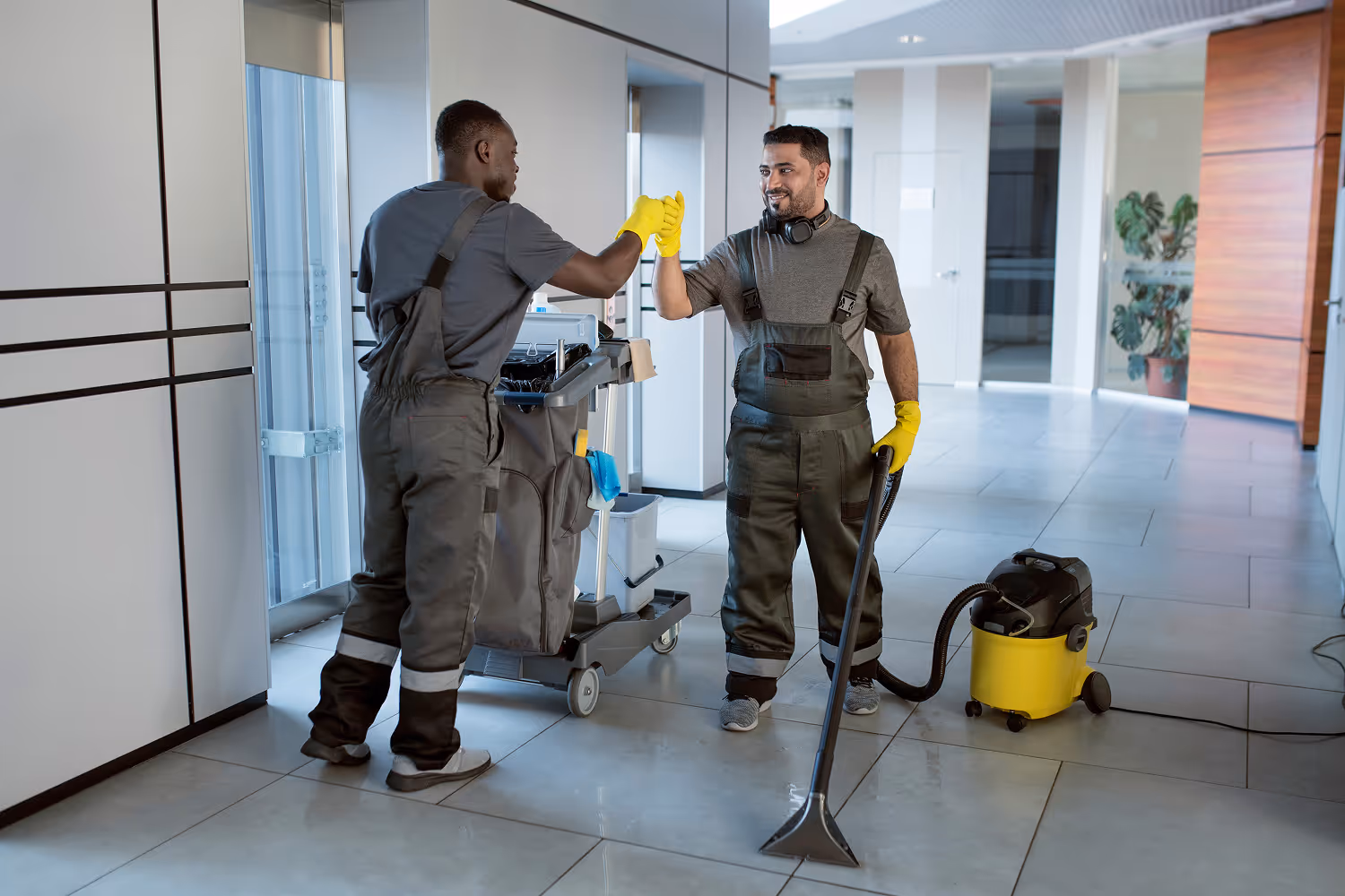 Professional cleaning team in uniforms performing commercial floor cleaning with vacuum and janitorial equipment in modern office building.