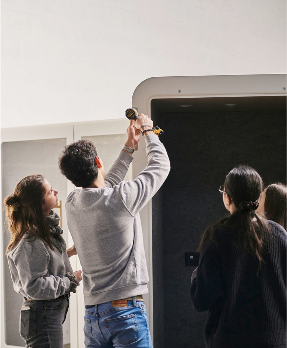 Un homme utilise une perceuse électrique pour travailler sur un élément mural tandis que trois femmes l'observent attentivement.