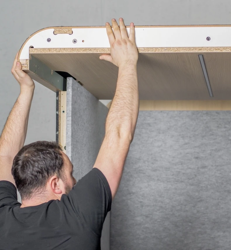 Installation d'une cabine acoustique blanche avec feutrine grise par un homme