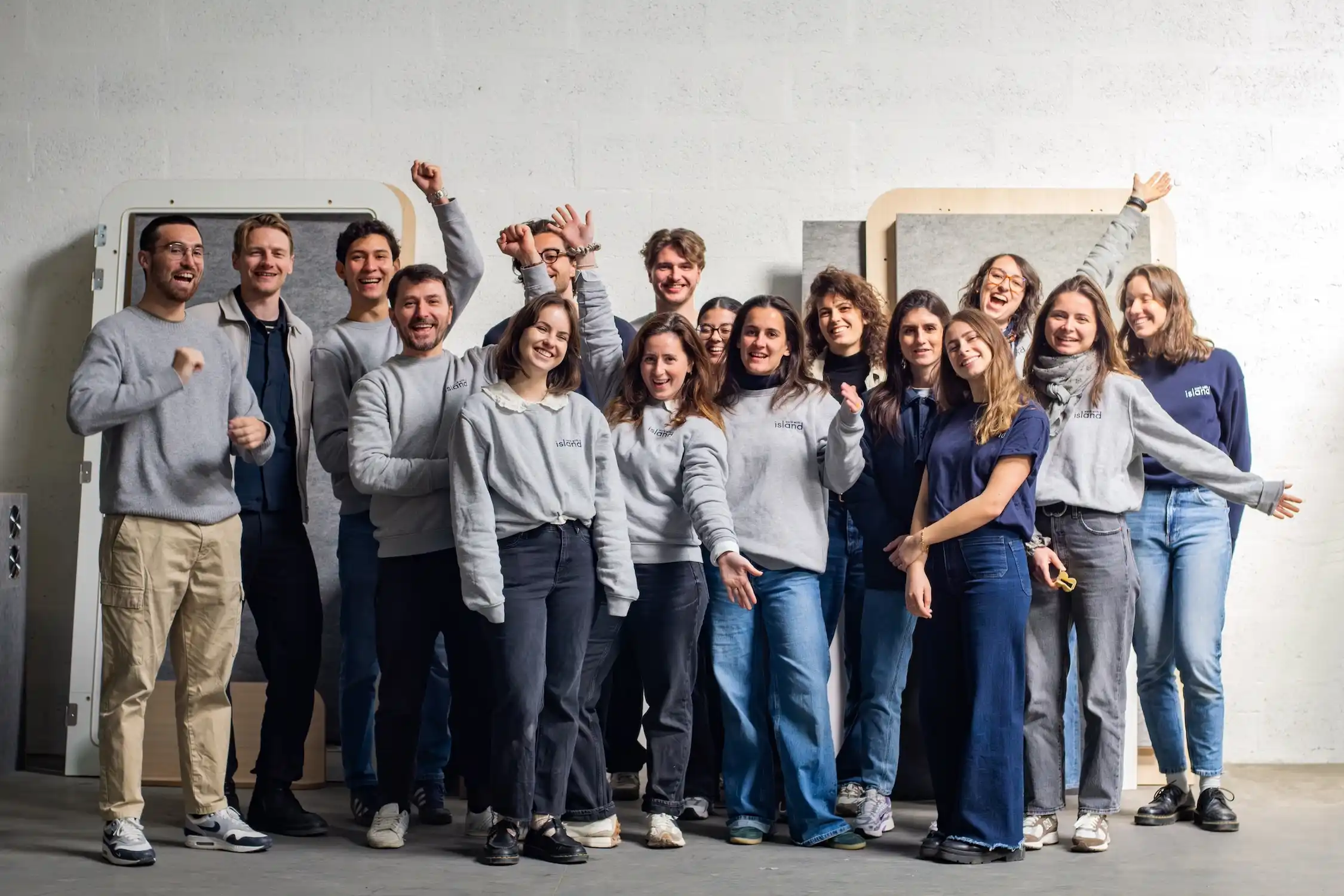 Photo de groupe de l'équipe Work With Island souriante devant des panneaux de cabines acoustiques en fabrication