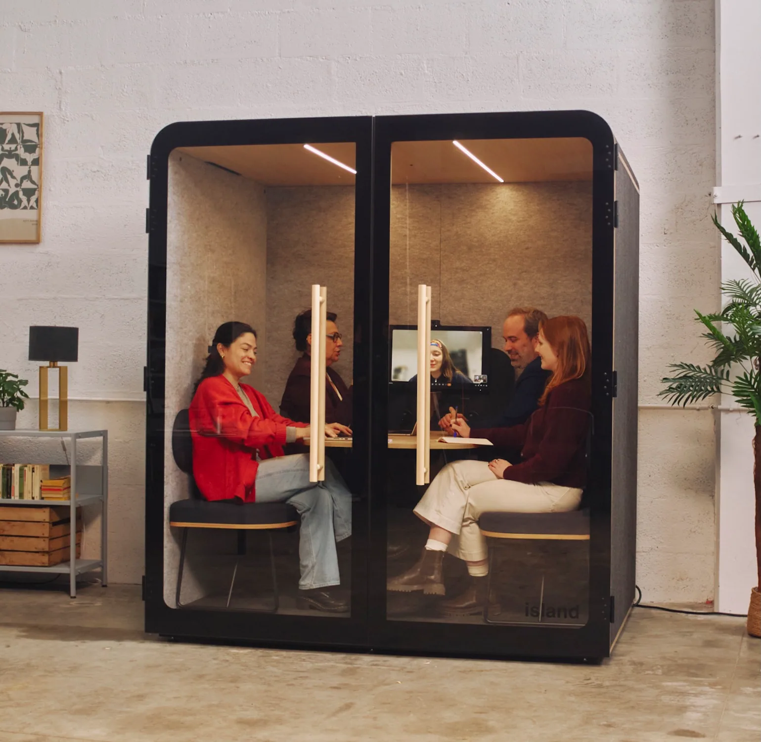 Quatre collaborateurs installés dans une cabine acoustique Island Duo, en réunion avec visioconférence