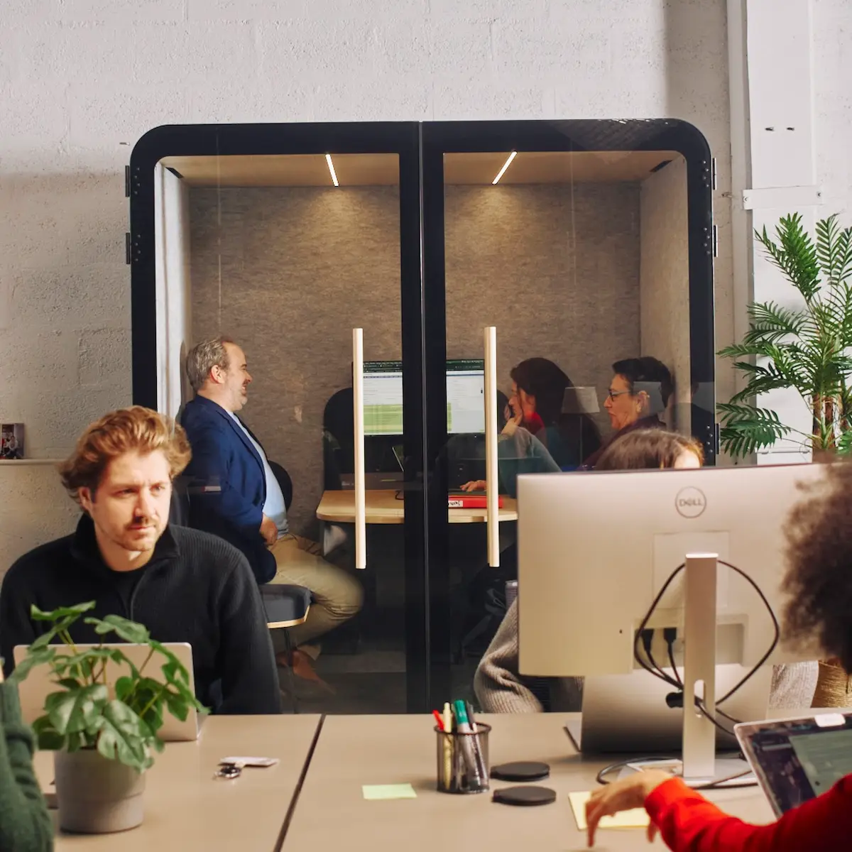 Cabine acoustique Island Quattro noire en open space, avec des collaborateurs travaillant à l'intérieur et autour