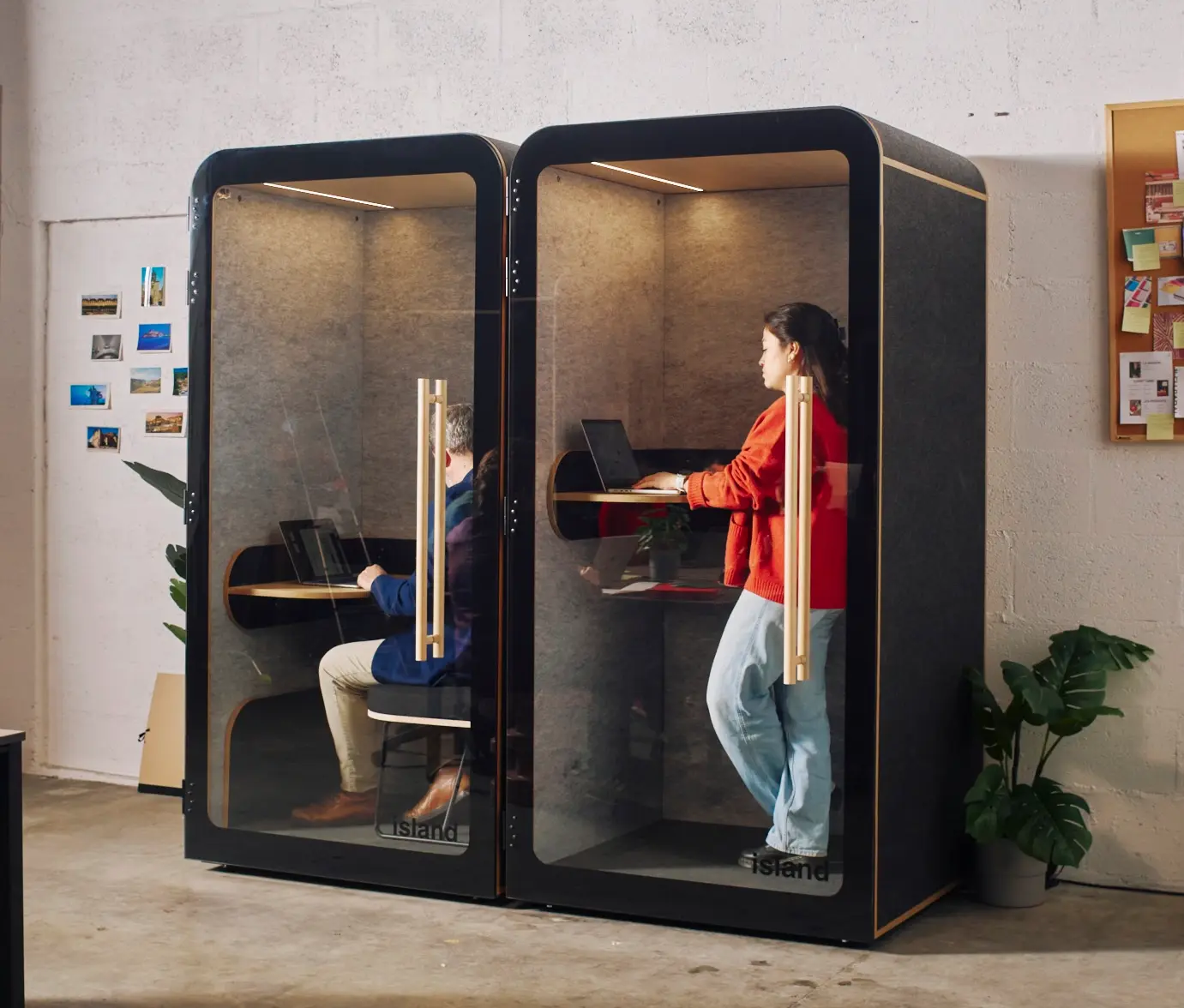 Deux cabines acoustiques Island Solo anthracite occupées, l'une assise et l'autre debout avec ordinateur portable