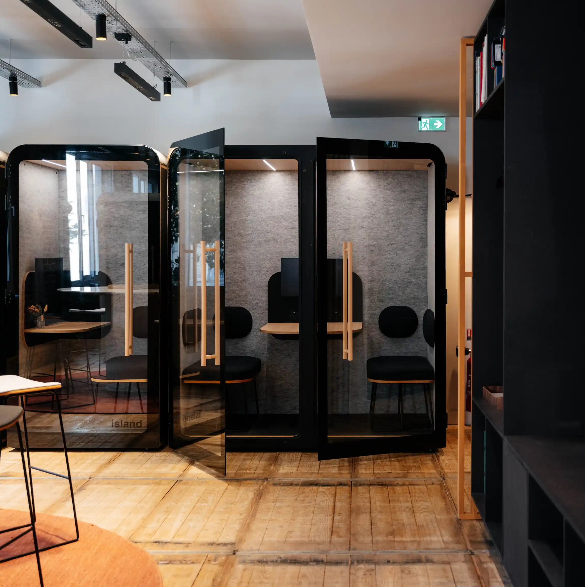 Cabines acoustiques Island Duo noires alignées dans un espace de travail au parquet bois