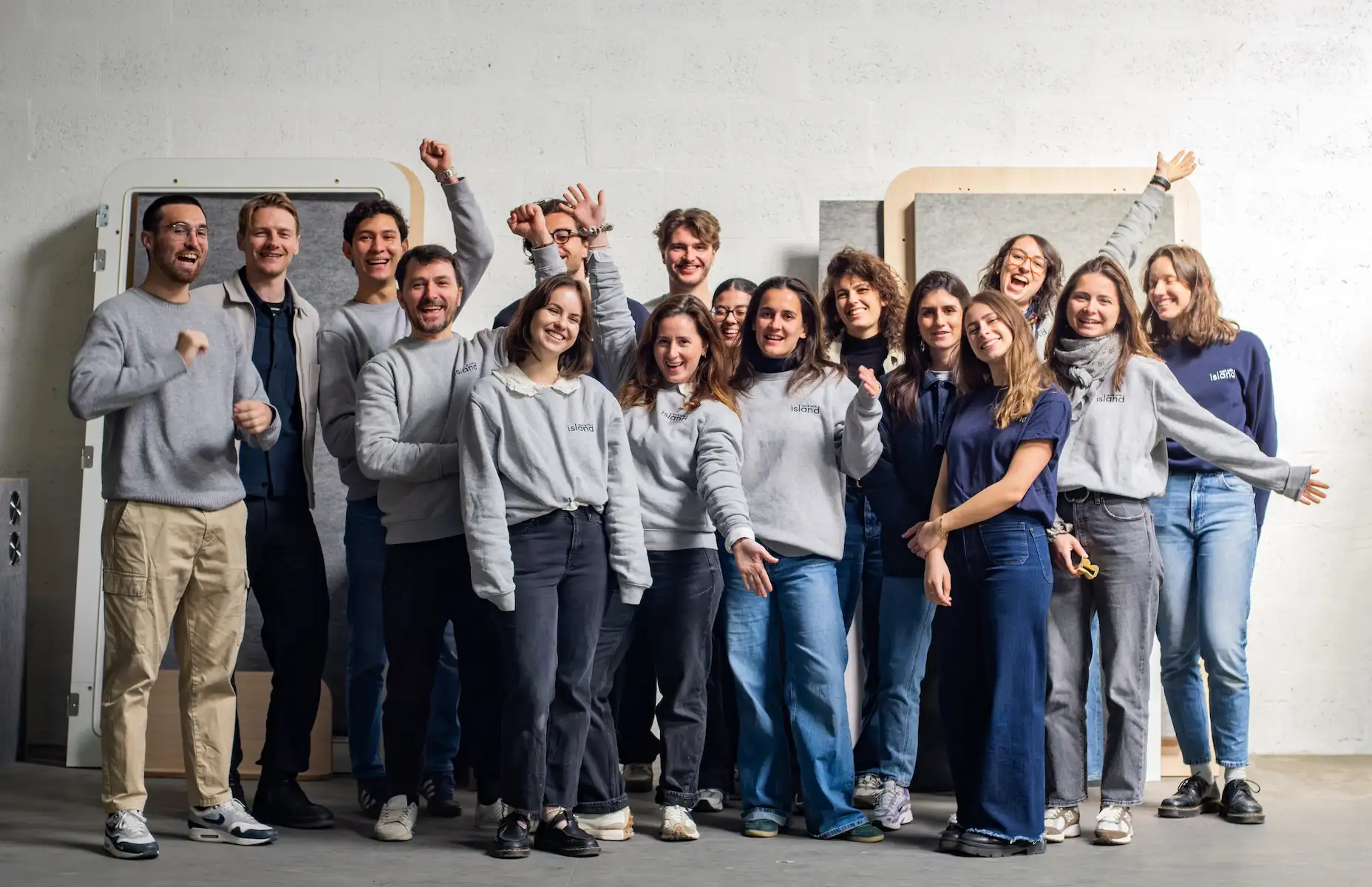 Photo de groupe de l'équipe Work With Island souriante devant des panneaux de cabines acoustiques en fabrication