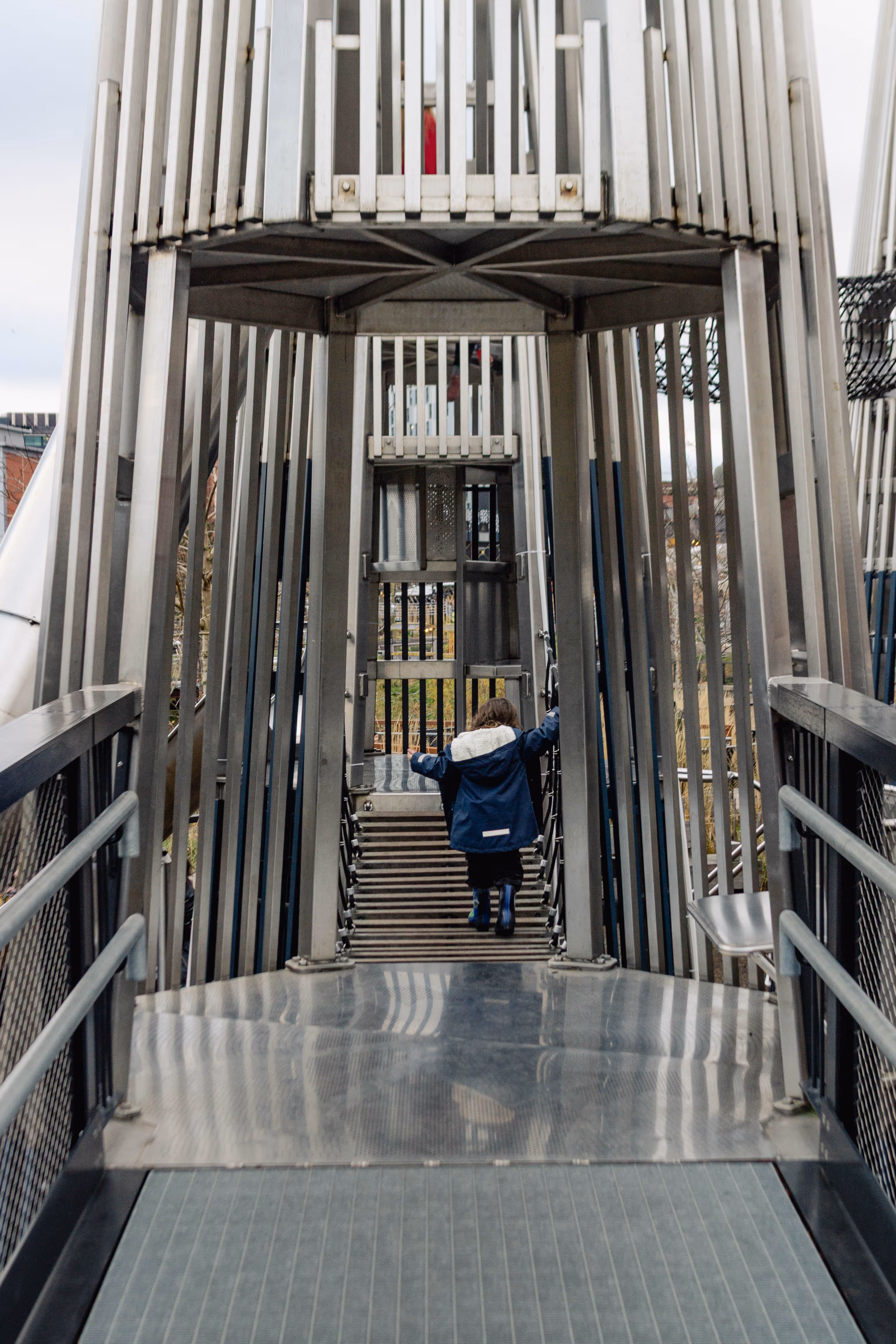 Child walking across suspended bridge between playground towers in adventure play structure