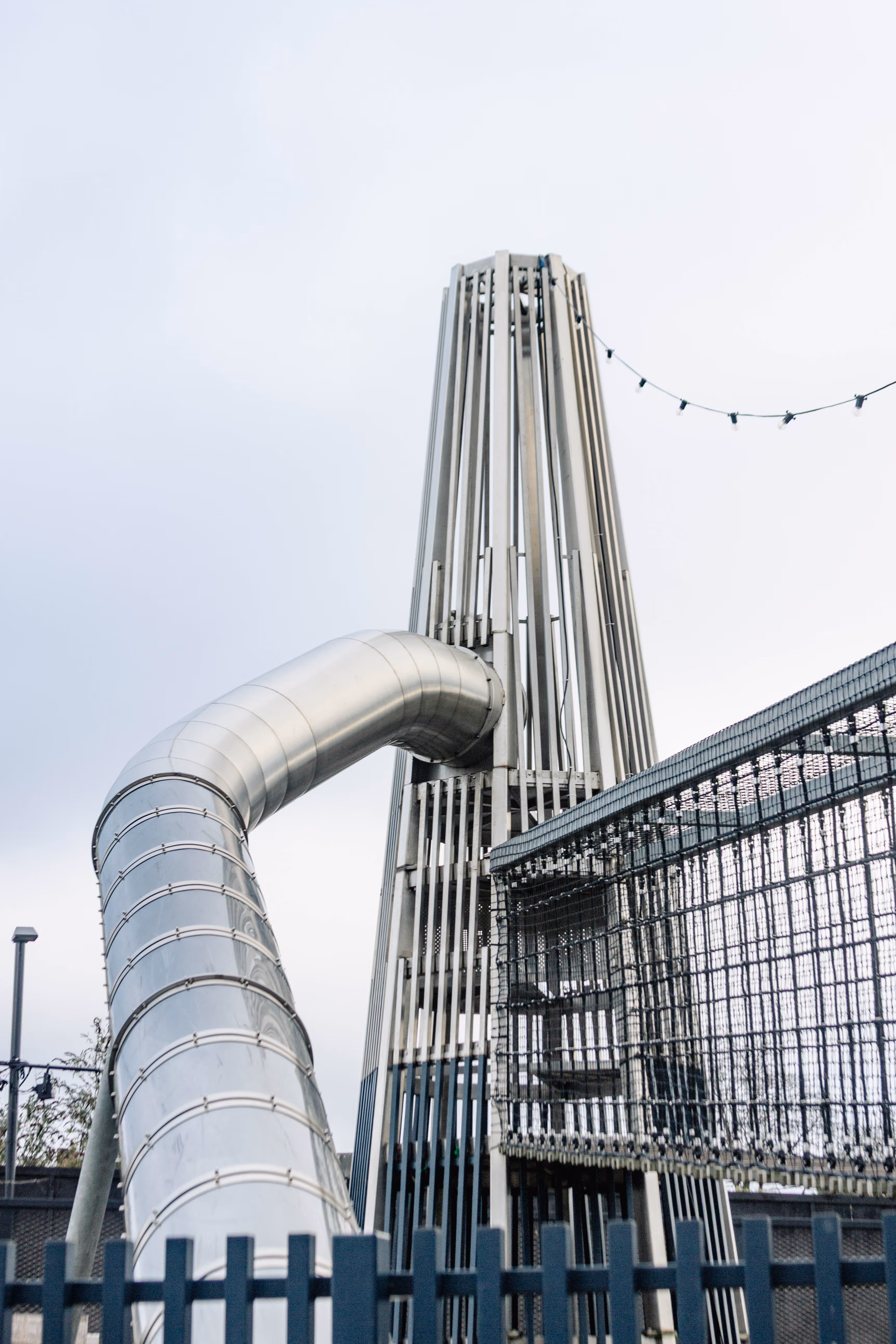 Adventure playground chimney tower design combining slide descent and elevated bridge access