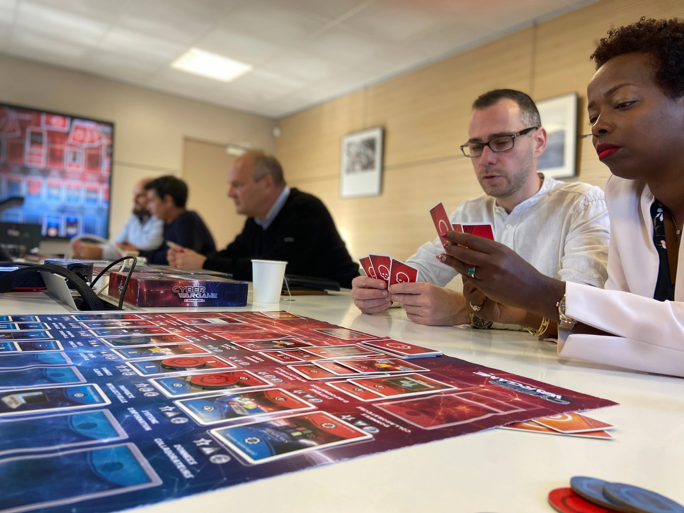 People seated around a table playing the board game Cyber War Game with cards and game pieces.