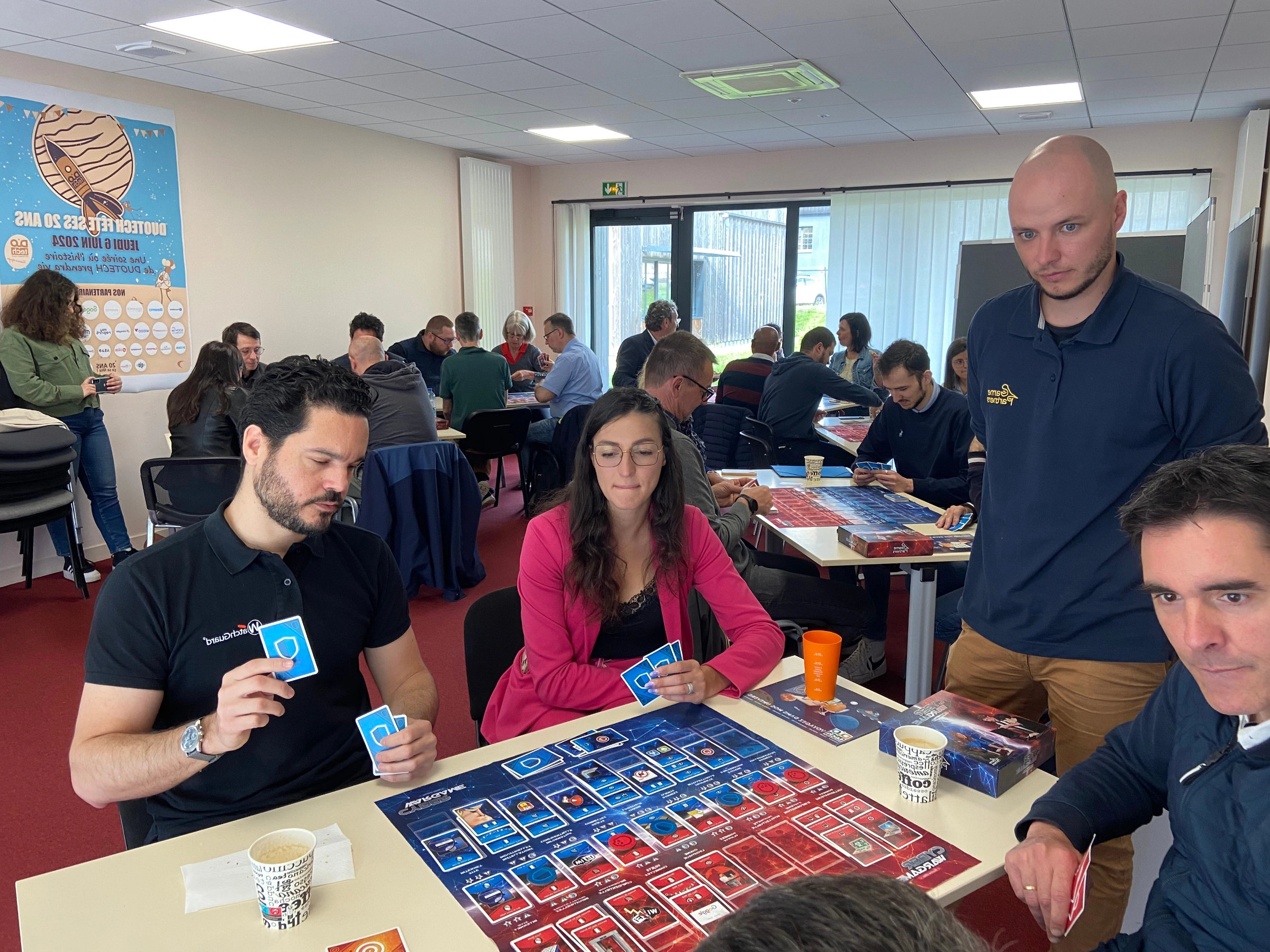People sitting and standing around tables playing a board game in a brightly lit room.