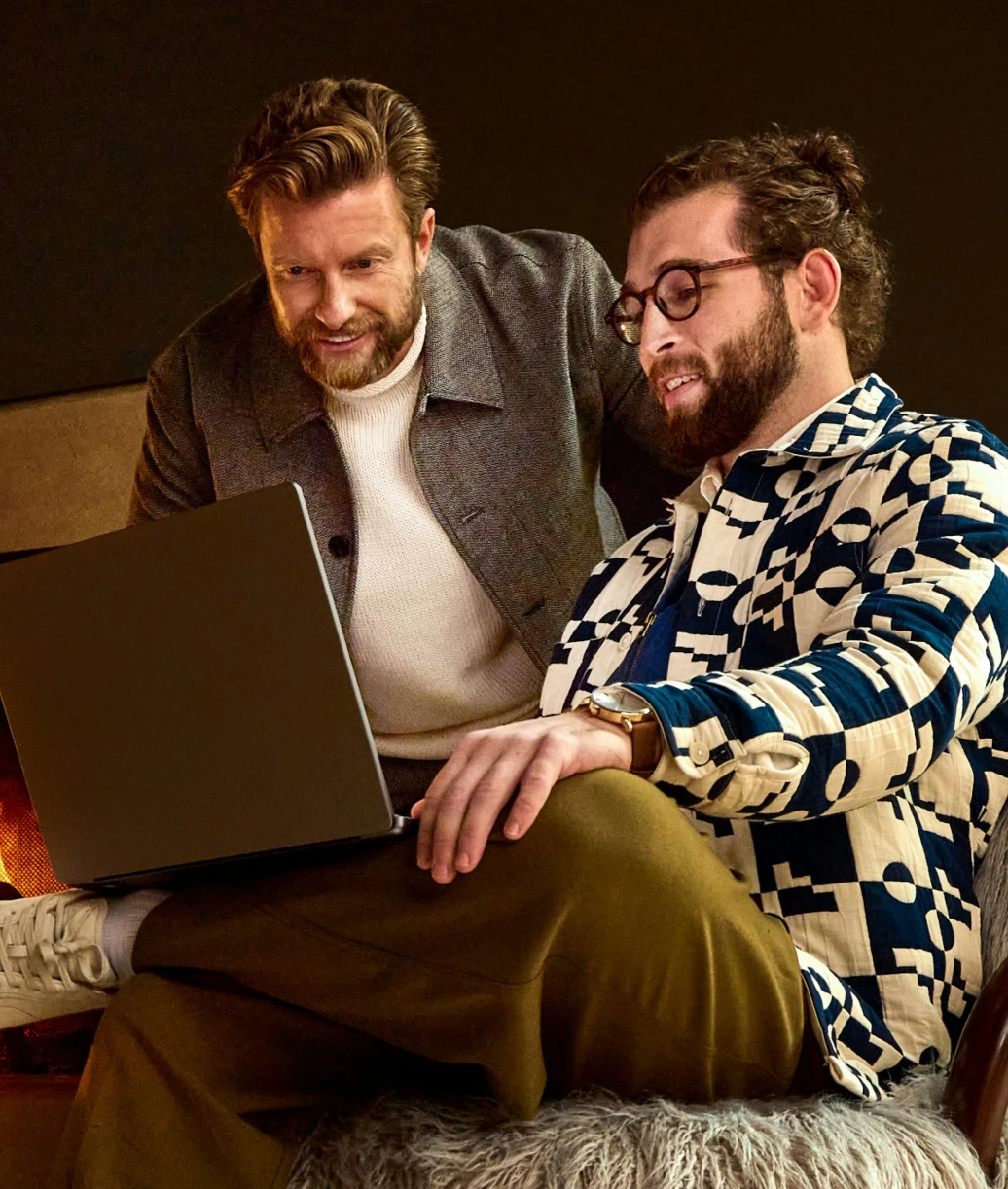 Deux hommes souriants assis ensemble regardant un ordinateur portable dans une ambiance chaleureuse.