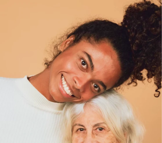 Jeune femme souriante posant sa tête sur la tête d'une personne âgée aux cheveux blancs.