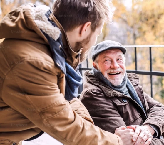 Un homme plus jeune tient la main d'un homme plus âgé souriant, tous deux habillés chaudement en hiver.