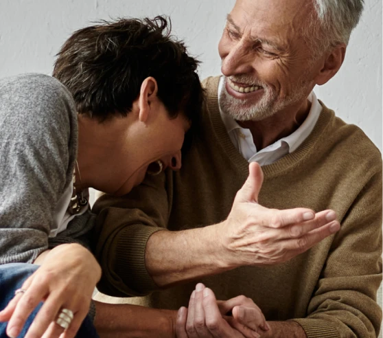 Un homme plus âgé et une femme rient ensemble dans un moment de complicité chaleureuse.