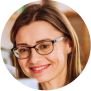 Portrait d'une femme souriante portant des lunettes et des boucles d'oreilles, avec des cheveux châtain clair et un maquillage naturel.