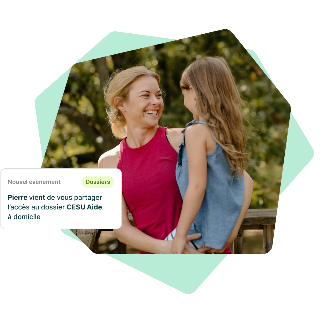 Une femme souriante en débardeur rose tient une petite fille aux cheveux longs portant un haut bleu, dans un cadre extérieur verdoyant.