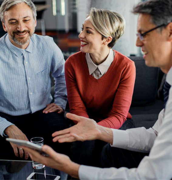 Trois professionnels souriants discutent ensemble, un homme tenant une tablette pour montrer quelque chose aux deux autres.