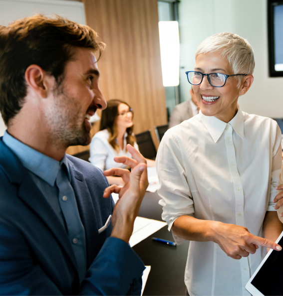 Deux collègues souriants discutant dans un bureau, une femme montre une tablette tactile à un homme.