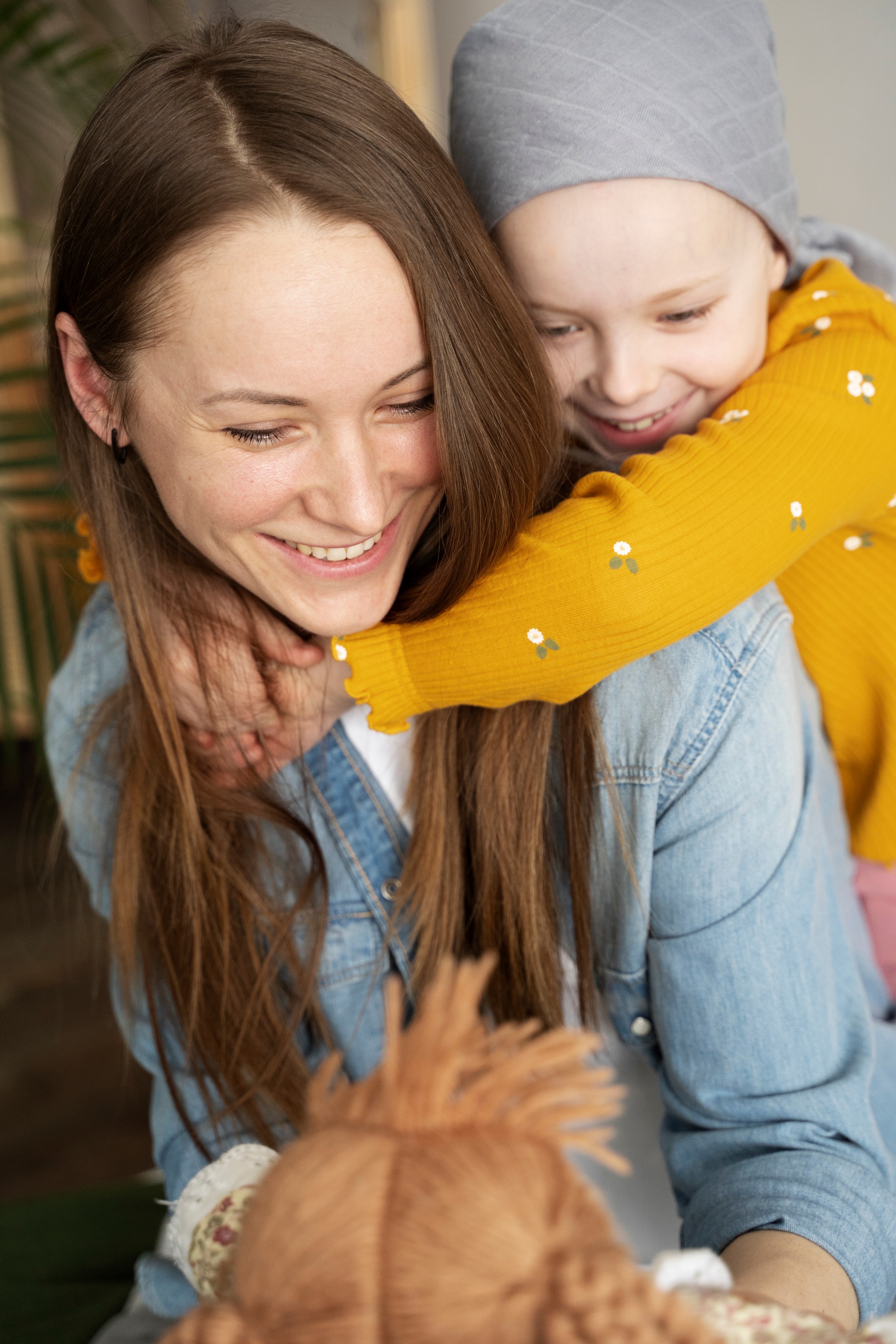 Une femme souriante en veste rose pointe vers l'appareil photo à côté d'une jeune fille avec trisomie 21 portant un chapeau vert et un sweat beige, tenant un vélo.