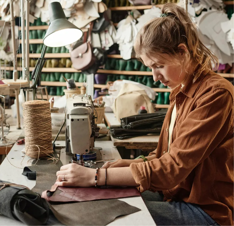 A woman using a sewing machine with shelves and materials behind her