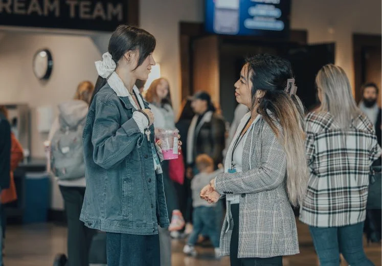 Two colleagues talking in office with team in background