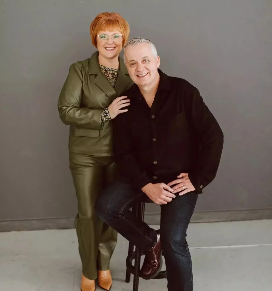 Smiling middle-aged couple in olive green and black outfit posing together