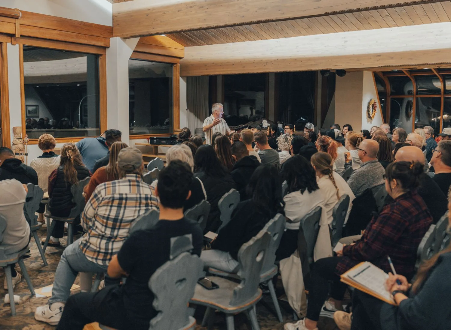 Crowded room with speaker presenting to attentive audience in wooden-paneled space