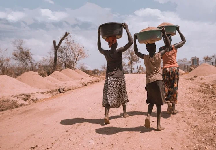 Women carrying water basins on heads walk along dusty rural road