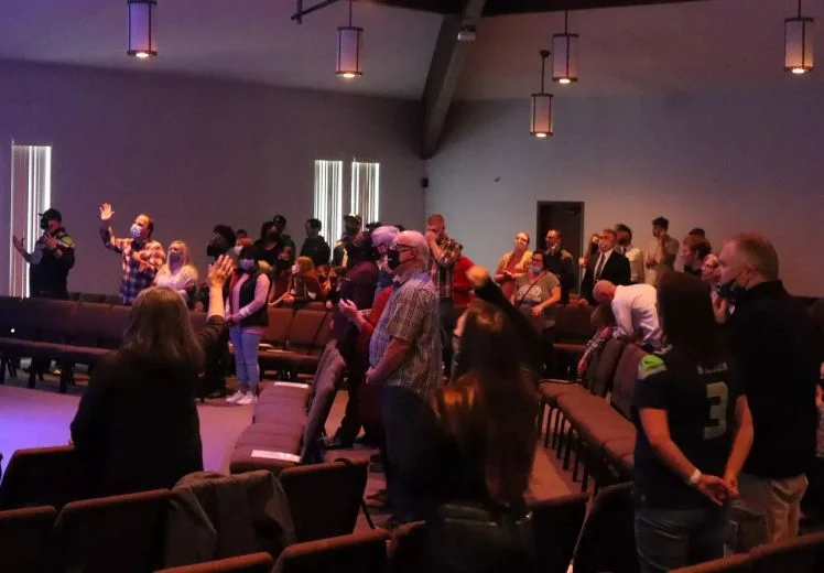 Diverse audience standing and sitting in dimly lit church or conference room