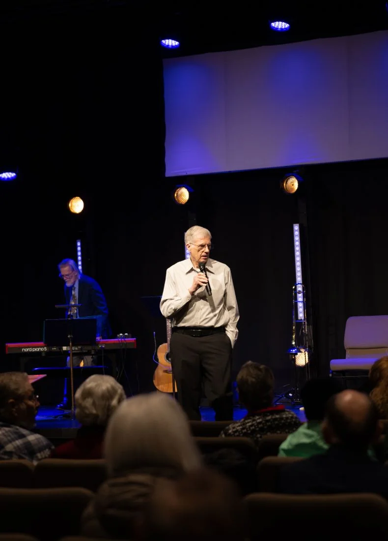 Older speaker on stage with microphone, blue and yellow stage lights