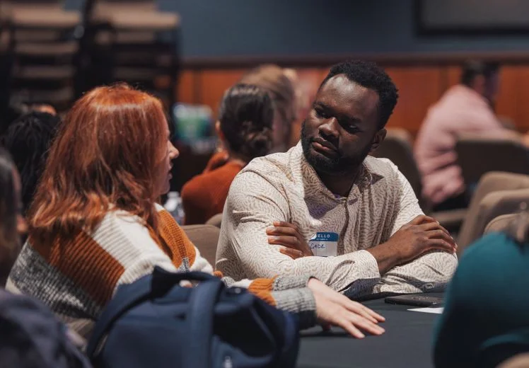 Two people in knit sweaters having an engaged conversation at a meeting