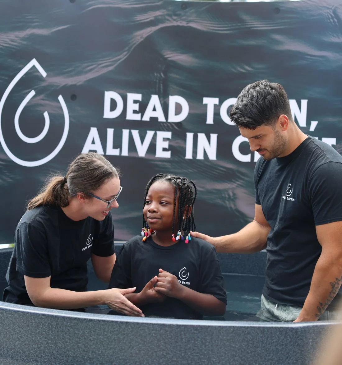 Team members in black shirts standing near "Dead to..." campaign backdrop