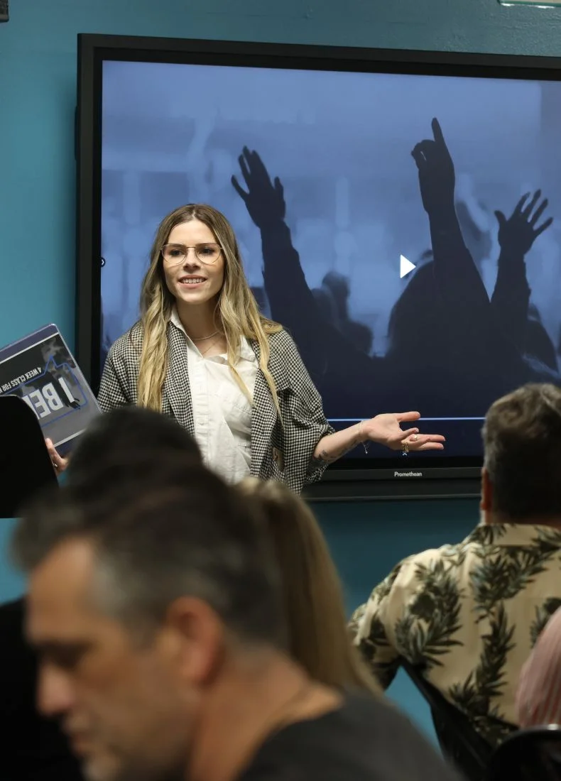 Woman presenting with raised hands on screen behind her