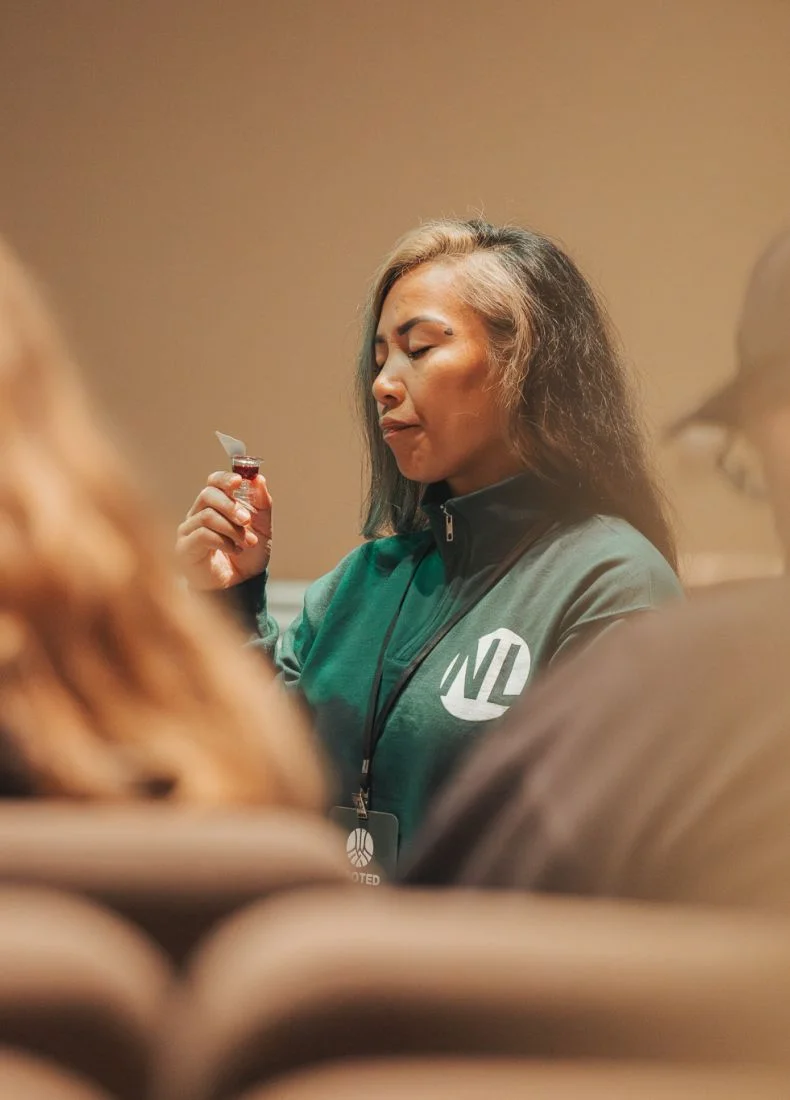 Woman in green jacket smelling small bottle with closed eyes