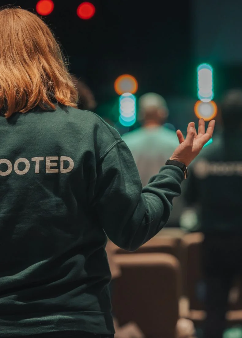 Person with "VOTED" jacket raising hand at colorful blurred lights