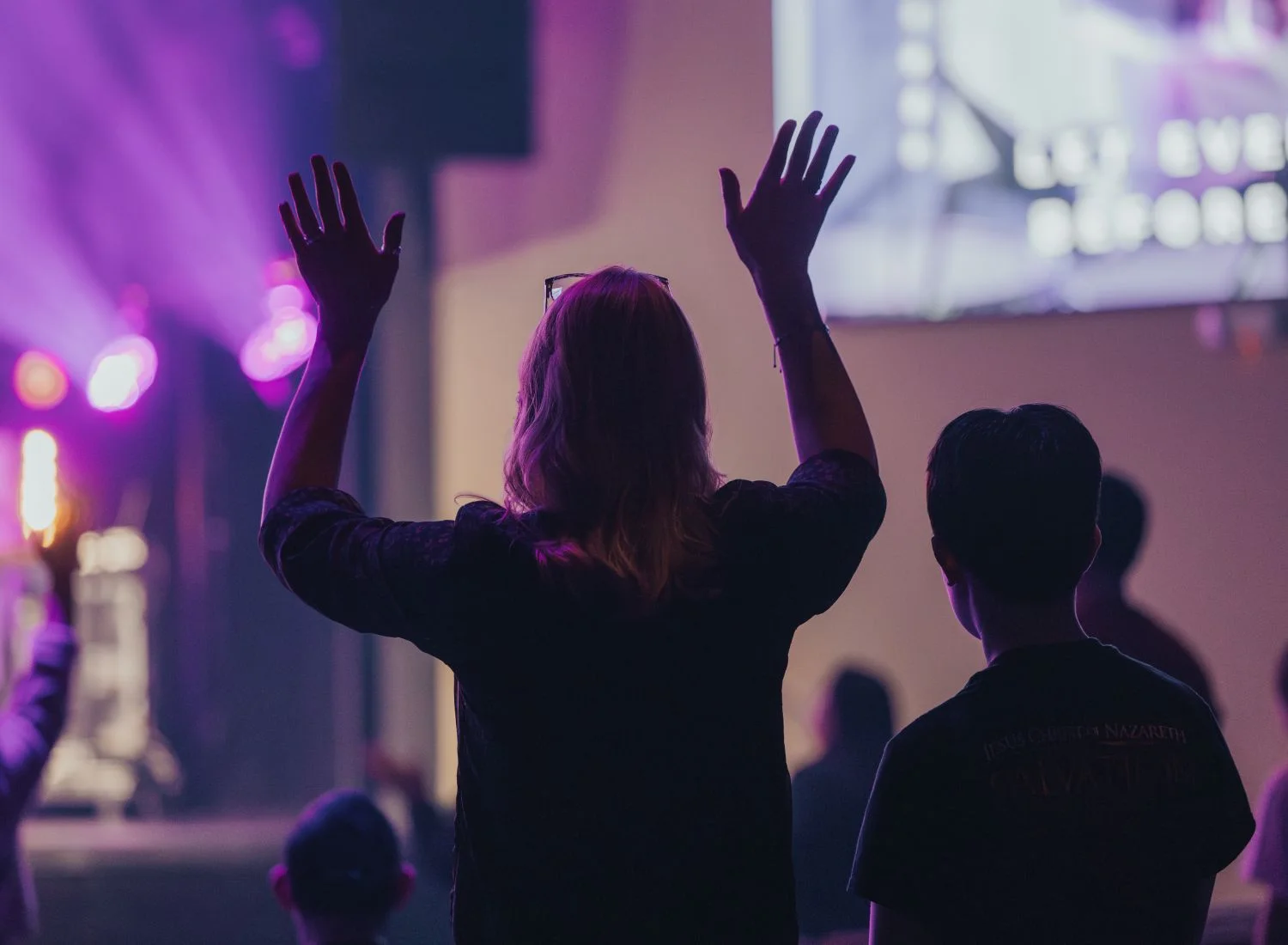 Audience raises hands at concert or worship event with purple lighting