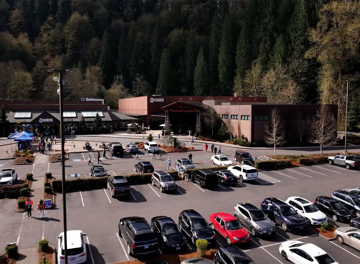 Busy church parking lot with cars and people, surrounded by forest trees