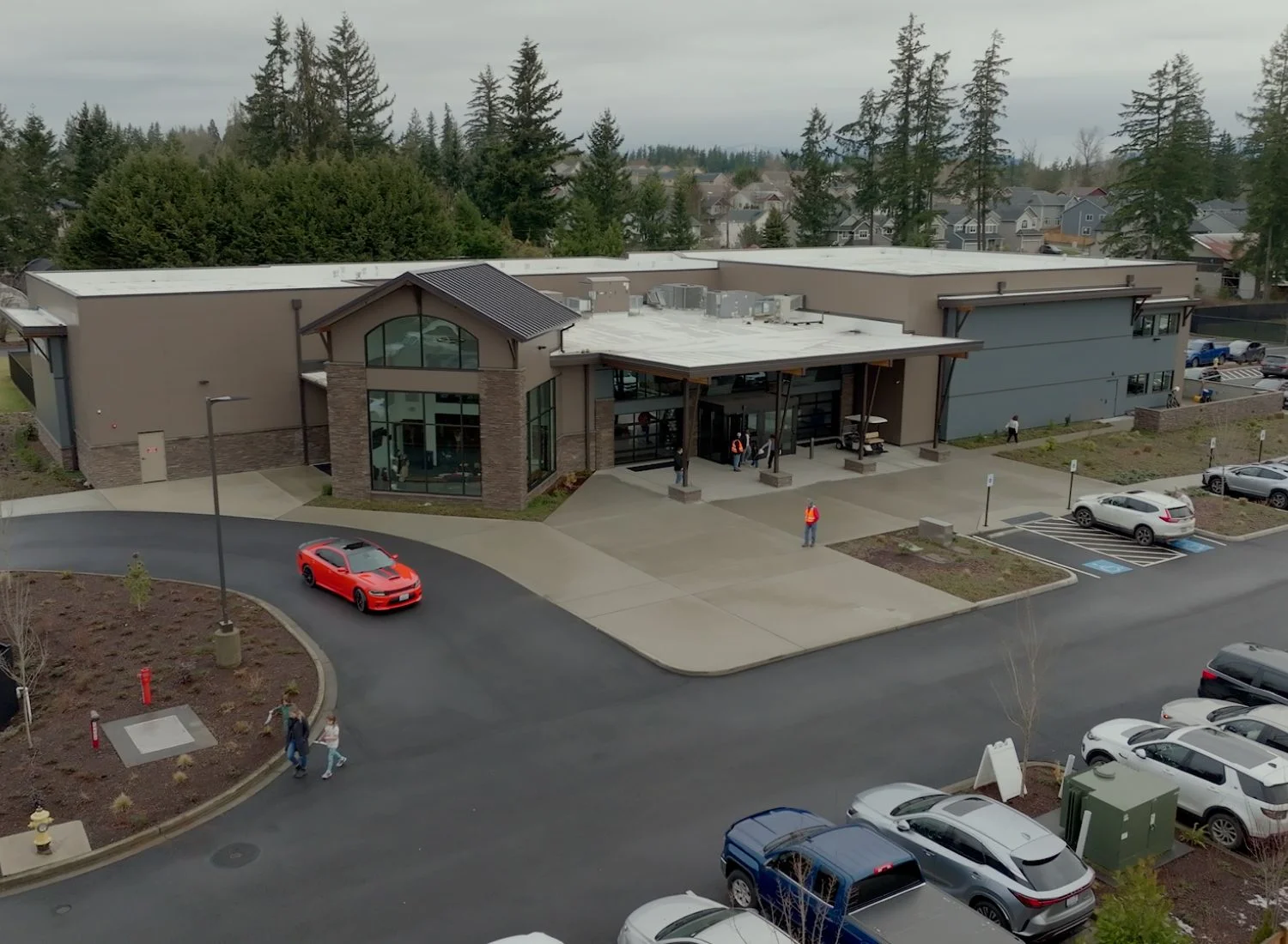 Modern building with parking lot, red car, and pine trees in background