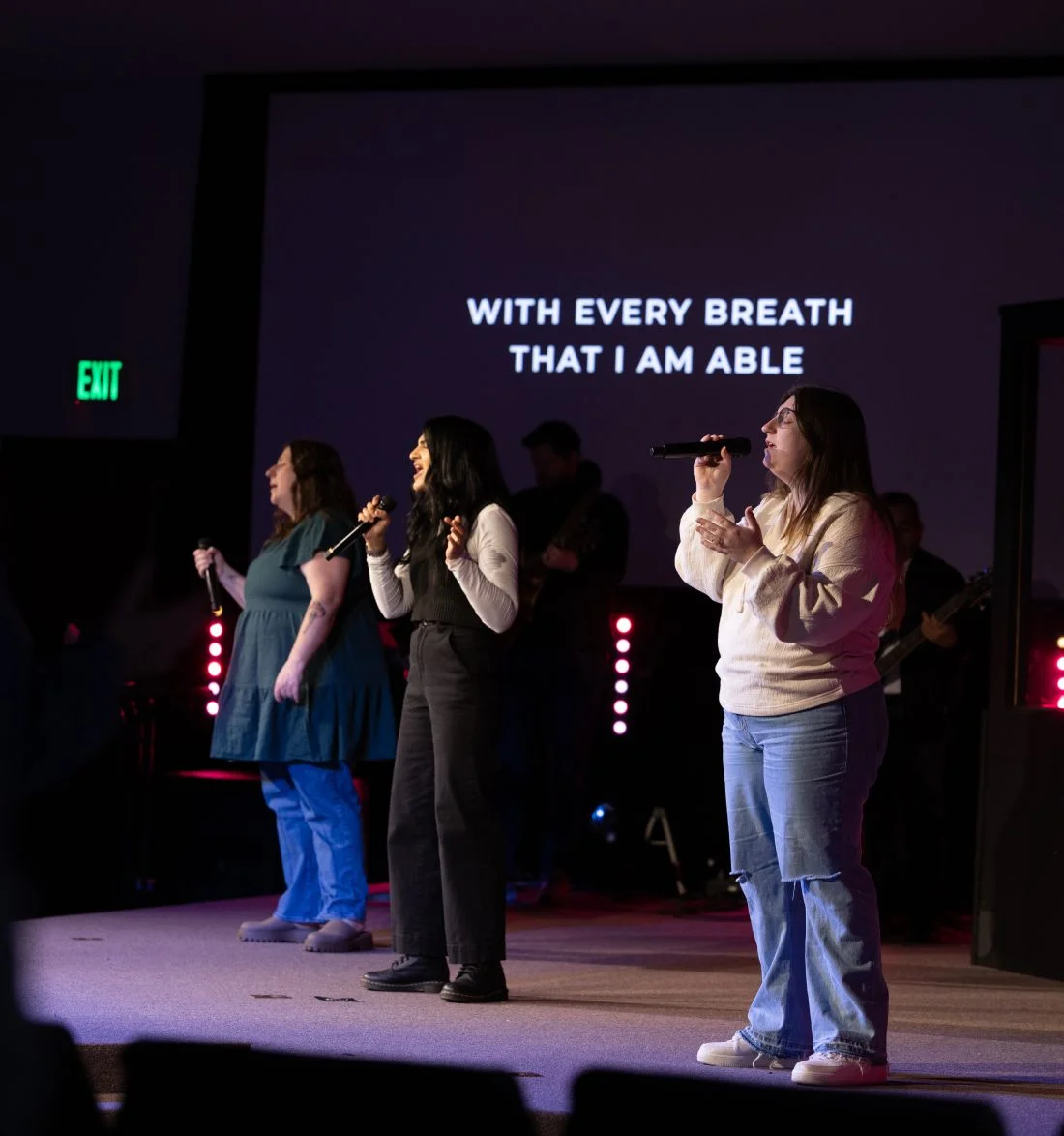 Three singers performing on stage with inspirational text backdrop