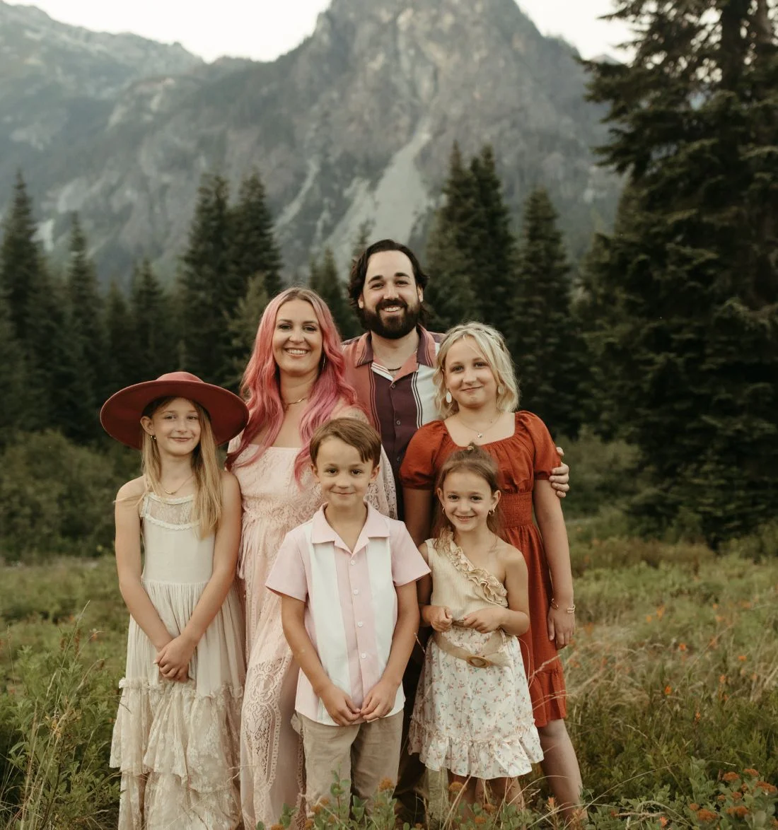 Family of six posing together in mountain meadow with forest backdrop