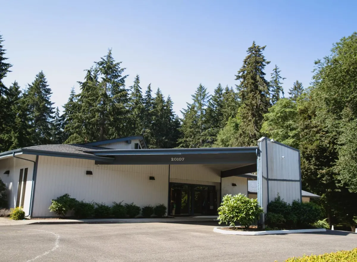 Modern white building with large windows surrounded by evergreen trees