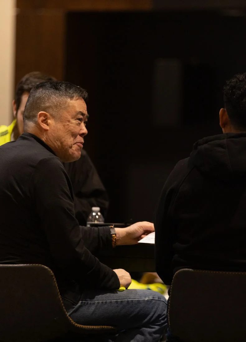 Person in black attire sitting at a meeting with others nearby