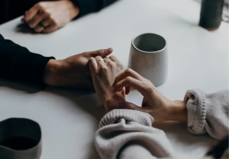Hands holding each other gently at a table with coffee mugs