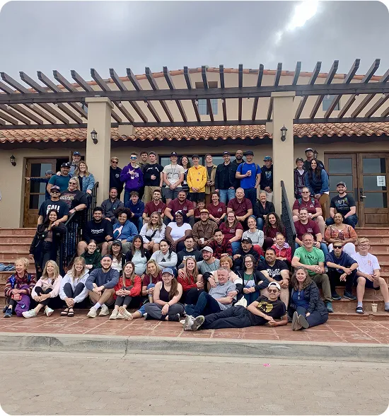 Large group photo of people gathered on steps under pergola structure
