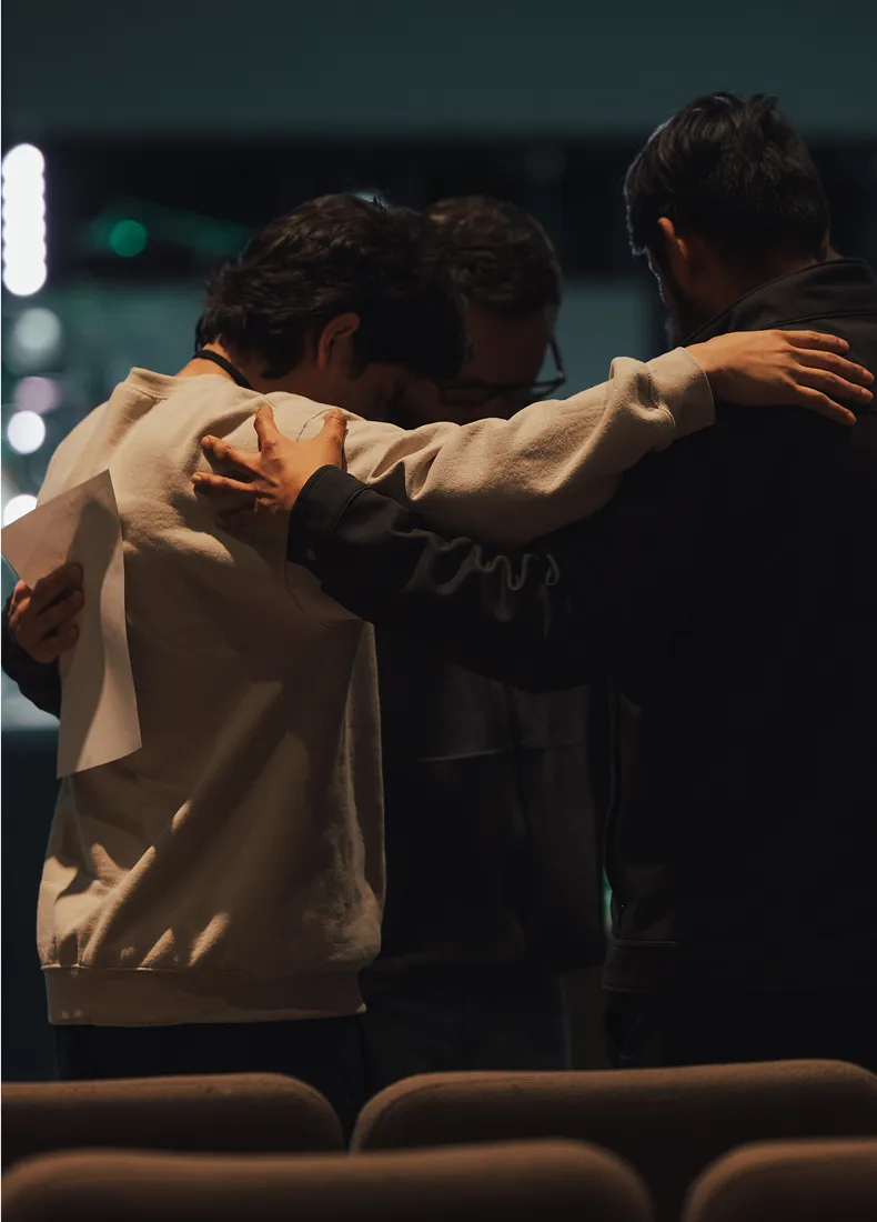Two people hugging from behind in a dimly lit theater or auditorium