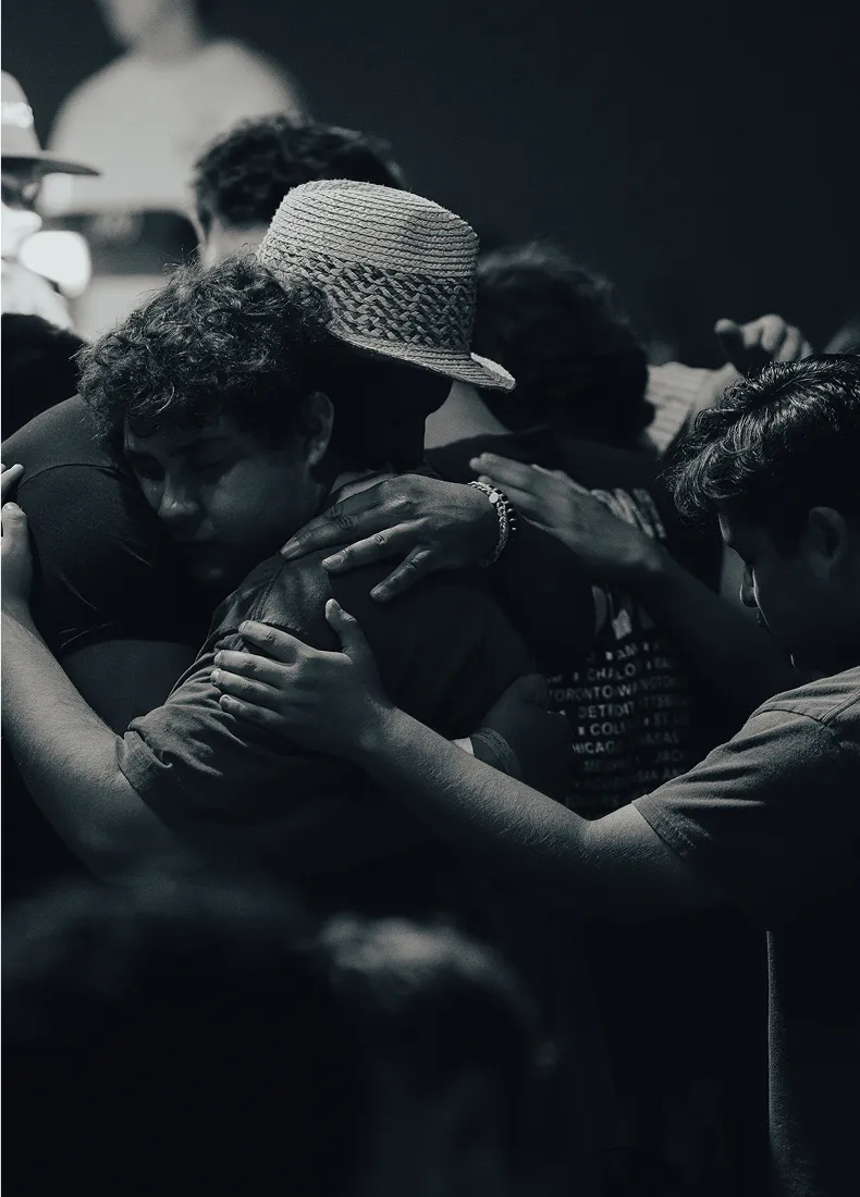 Emotional group hug with people embracing, one wearing a woven hat