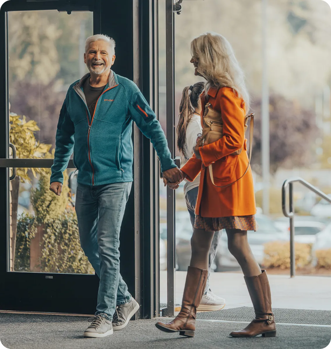 Older couple holding hands, smiling while walking through glass doorway