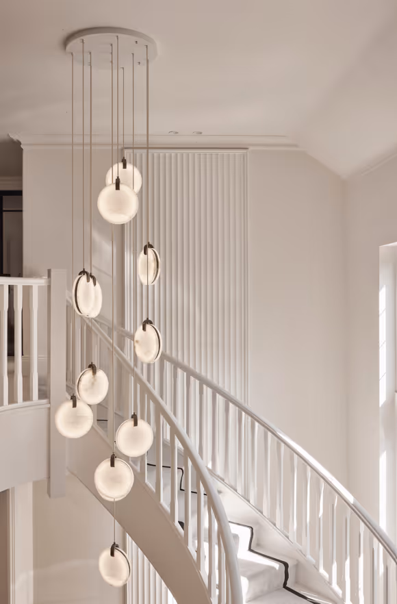 Modern white spiral staircase with vertical railing and a hanging chandelier featuring multiple round glowing lights.